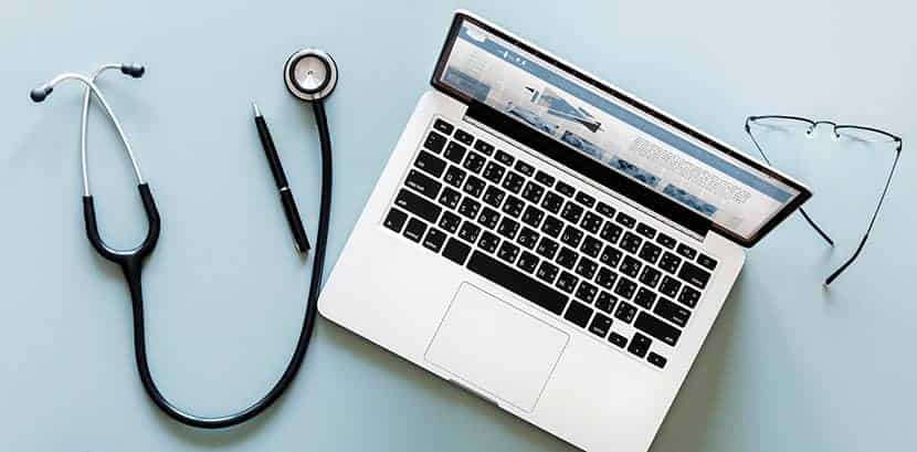 doctors laptop open with glasses next to it